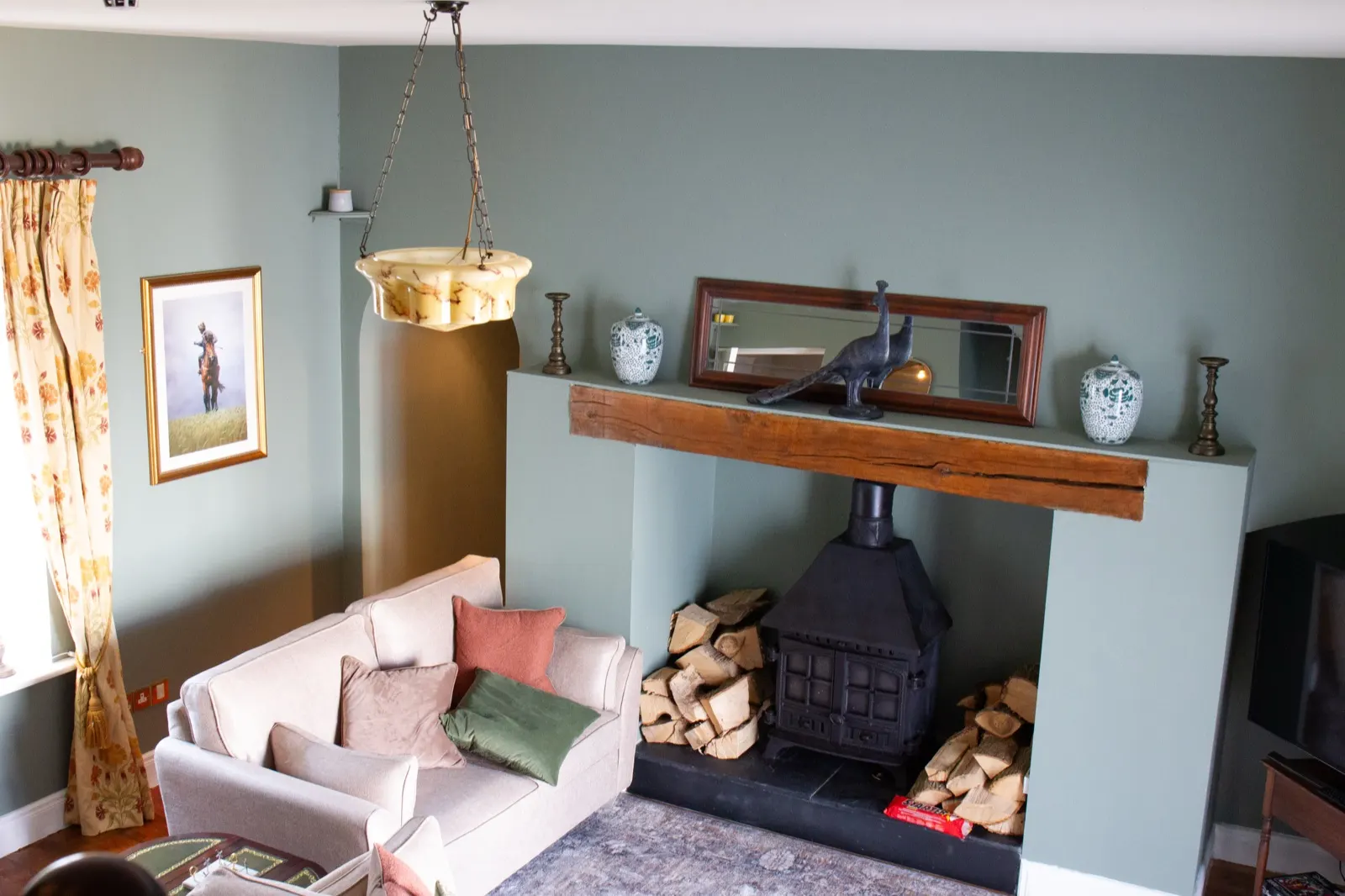 Sitting room with a wood-burning stove, stacked logs and sofas either side of the hearth